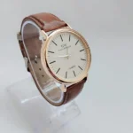 Minimalist quartz watch with gold-tone case and brown leather strap on white background