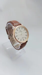 Minimalist quartz watch with gold-tone case and brown leather strap on white background